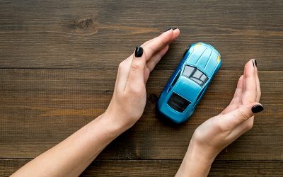 Car insurance concept. Safety of auto. Car toy in female hands on dark wooden background top view.